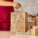 A natural kraft paper shopping bag with handles and a modern holiday print featuring trees, candy canes, and snowflakes.