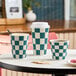 A set of navy and cream checkered double wall ripple paper hot cups in various sizes, with one cup featuring a white lid.