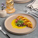 A tan round porcelain plate with a raised rim, shown with food served on it.