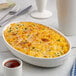 An ivory oval porcelain casserole bowl filled with baked macaroni and cheese, garnished with herbs.