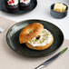 A black round porcelain coupe flat plate with a bagel and cream cheese served on it.