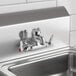 A wall-mounted chrome service sink faucet with two lever handles, a vacuum breaker, and adjustable arm centers.