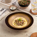 A brown round porcelain coupe deep plate with a wide rim, shown as part of a table setting.