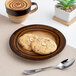 A brown round wide rim porcelain flat plate with two cookies on it.