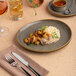 An oval brown porcelain platter with an irregular raised rim, featuring a serving of rice and shrimp.