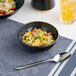 A black round embossed porcelain coupe bowl filled with a colorful salad.