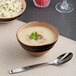 A brown round irregular tapered porcelain soup bowl filled with creamy soup and garnished with herbs.