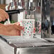 A paper hot cup with a modern Christmas print being filled at a coffee machine.