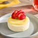 A small round yuzu cheesecake topped with sliced strawberries, served on a gray plate.