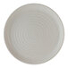 A round, light-colored porcelain plate with a subtle speckled pattern and concentric circular ridges.
