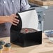 A black bakery box with an open lid containing a cake, displayed on a kitchen counter.