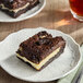 A chocolate brownie bar with a creamy filling and Oreo cookie pieces on top, served on a white plate.