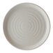 A round, light-colored porcelain plate with a subtle speckled pattern and concentric circular ridges.