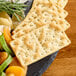 A set of rectangular gluten-free rosemary table crackers arranged on a slate serving board with assorted fruits and herbs.