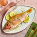 A whole Caribbean red snapper served on a white plate with lemon slices and herbs.