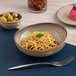 A beige round slanted porcelain coupe bowl filled with pasta, placed on a table setting.