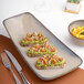 A large beige asymmetric rectangular porcelain platter with three pieces of avocado toast, displayed on a table setting.