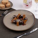 A beige round slanted porcelain coupe flat plate with a dessert arrangement, shown on a table setting.