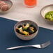 A small beige round porcelain coupe bowl filled with blackberries, lemon wedges, and walnuts.