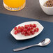 A small, ivory, asymmetric rectangular porcelain coupe plate holding red currants.