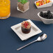 A small ivory square porcelain plate with an asymmetric rim, shown holding a dessert.