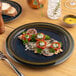A blue round porcelain coupe flat plate with a decorative food presentation.
