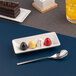 A small ivory rectangular porcelain bowl with a wide rim, shown holding four colorful chocolates.
