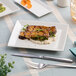 A rectangular ivory porcelain coupe platter with a modern design, shown holding a plated dish.
