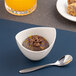 A small ivory porcelain bowl with a curved rim, filled with chocolate mousse and garnished, accompanied by a spoon.