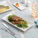 A rectangular ivory porcelain coupe platter displaying grilled skewers and greens.