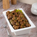 A rectangular ivory porcelain deep platter filled with seasoned roasted baby potatoes and garnished with green herbs.