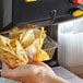 A hand pouring Muy Fresco cheddar cheese sauce onto a container of chips.