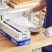 A box of Choice 18-inch by 2000-foot foodservice cling film with a serrated cutter being used to cover a bowl.