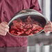 A person holding a stainless steel bowl filled with marinated raw meat.