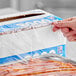 A box of foodservice plastic wrap film with a serrated cutter being used to cover food.