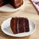 A slice of layered chocolate cake with chocolate frosting on a white plate.