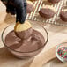 A bowl of melted milk chocolate compound coating being used to dip cookies, with finished chocolate-coated cookies and sprinkles nearby.