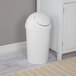 A white round wastebasket with a swing-top lid.