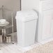 A white rectangular wastebasket with a swing-top lid placed in a kitchen setting.
