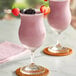 A glass of purple acai smoothie garnished with fresh berries and a strawberry slice, served on a coaster.