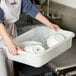 A person holding a Tablecraft white plastic bus tub full of dishes.