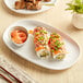 A white, irregular oval matte melamine coupe plate holding sushi rolls and a small bowl of pickled ginger.