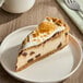 A slice of s'mores cheesecake with a graham cracker crust, chocolate chunks, and toasted marshmallow topping on a white plate.