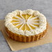 A pre-cut key lime pie cheesecake topped with whipped cream and served on a brown crust.
