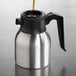 A stainless steel insulated coffee server with a black handle and lid, being filled with liquid.