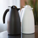 A black and a white plastic insulated coffee server with push-button lids.