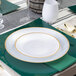 A round pearl white plastic plate with a gold band around the edge, placed on a green placemat.