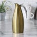 A vintage gold stainless steel insulated coffee carafe server with a sleek handle.