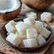 A wooden bowl filled with white coconut puree cubes, with a halved coconut in the background.
