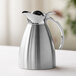 A polished stainless steel insulated carafe with a flip-top lid and handle.